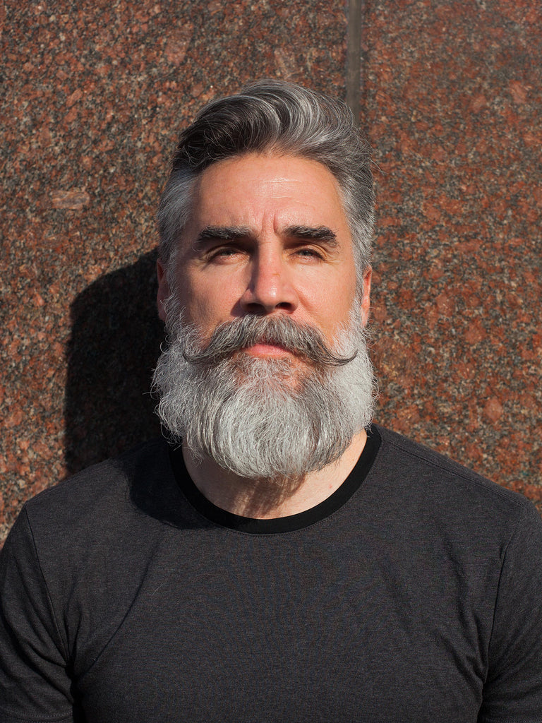 headshot of Greg Berzinsky with a silver Verdi beard and handlebar mustache
