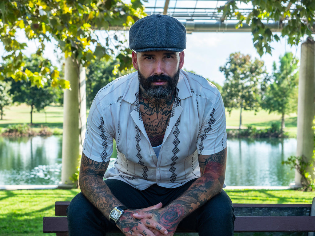 Carlos Costa with a short boxed beard and wearing a flat cap