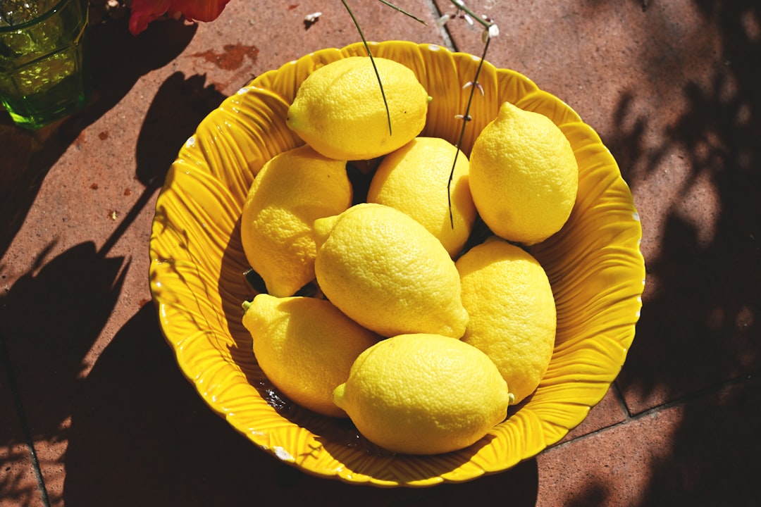 Fresh lemons in a yellow bowl highlighted in sunlight, illustrating natural ingredients in hydration trends.