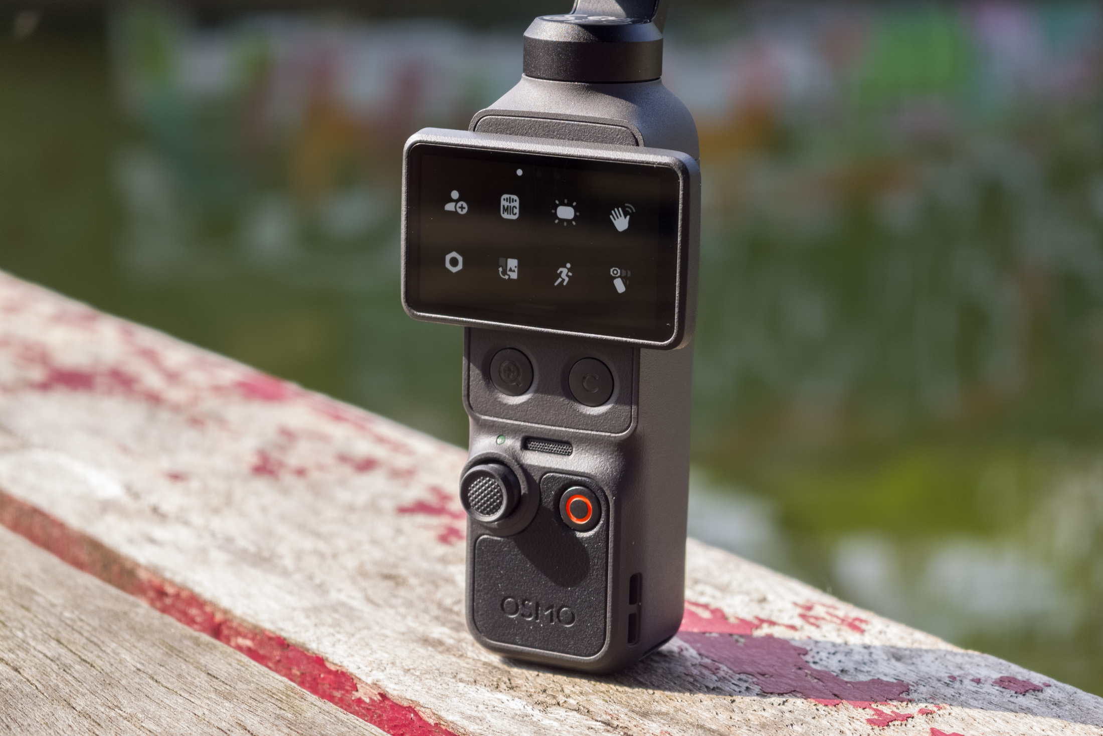 Photo of DJI Osmo Pocket 4 standing on a wooden table in front of a canal, showing the screen with the settings menu