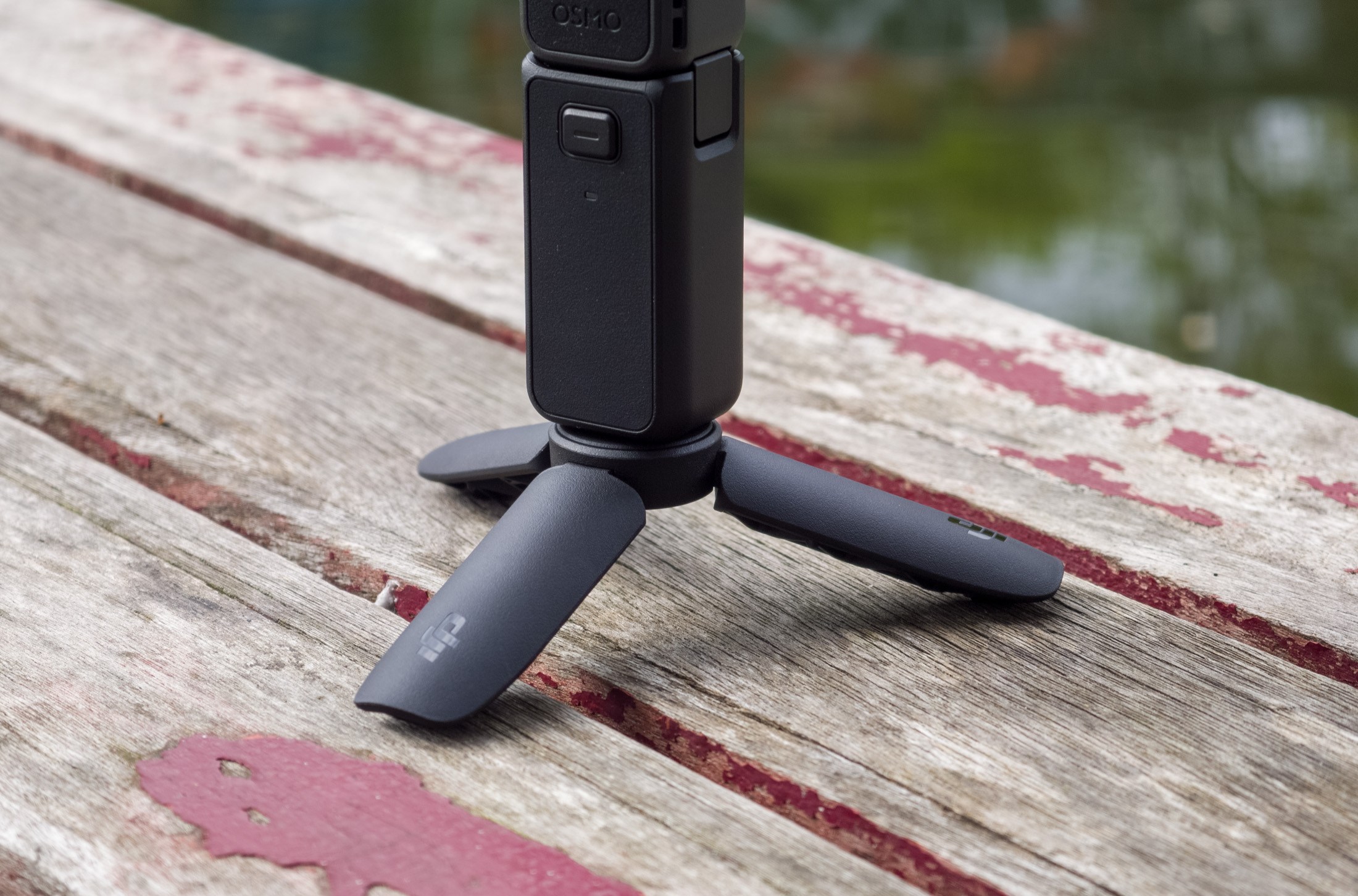 A photo of the DJI Osmo Pocket 4 tripod on a wooden table in front of a canal