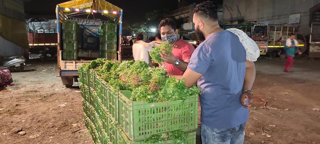 Meeshoite Rahul Akula, a meesho employee, at a marketplace at 3AM in the morning. Rahul is a brown, South-Asian man in a pink T-shirt talking to a vegetable wholesale seller who is selling coriander/
