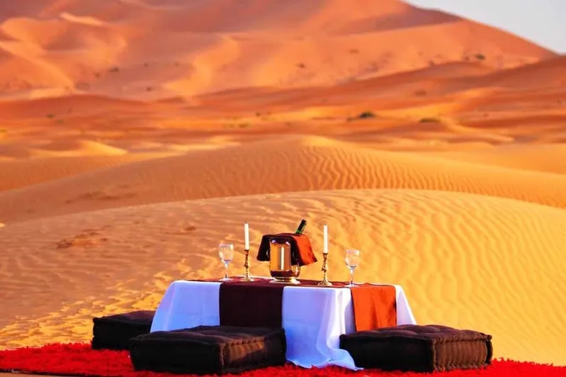 A romantic dinner set in the desert, featuring a table with candles and a backdrop of sand dunes and a sunset.