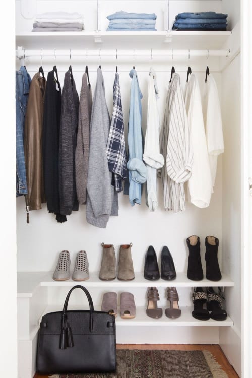 A wardrobe with various neatly organised clothes, shoes, and a bag.
